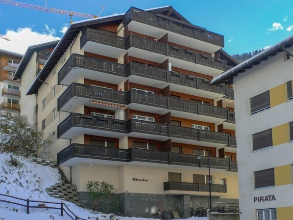 A multi-story hotel with balconies and a ski slope in the background.