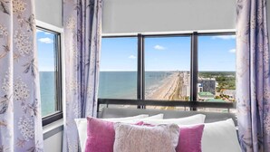A room with a large window offering a view of the beach and cityscape. - Palace 2305 (Myrtle Beach)