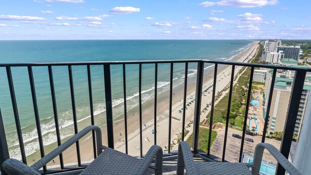 A balcony with a view of a beach and ocean, featuring a railing and a chair. - Palace 2305 (Myrtle Beach)