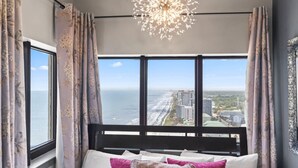 A bedroom with a large window, a bed, and a chandelier. - Palace 2305 (Myrtle Beach)