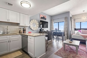 A modern kitchen with white cabinets, a central island, and a dining area with a table and chairs. - Palace 2305 (Myrtle Beach)