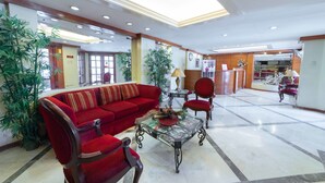 A lobby with a red sofa, a glass coffee table, and a red armchair. There are potted plants and a reception desk in the background. - RedDoorz @ The Manor Davao (Davao)