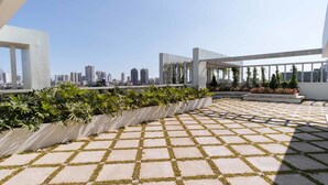 A rooftop terrace with a city skyline view, potted plants, and a patterned floor. - RedDoorz Premium @ Vista Heights Legarda (Manila)