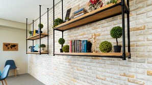 A room with a brick wall, two black metal shelves with books and plants, a blue chair, and a small globe map on the wall. - RedDoorz Premium @ Vista Heights Legarda (Manila)