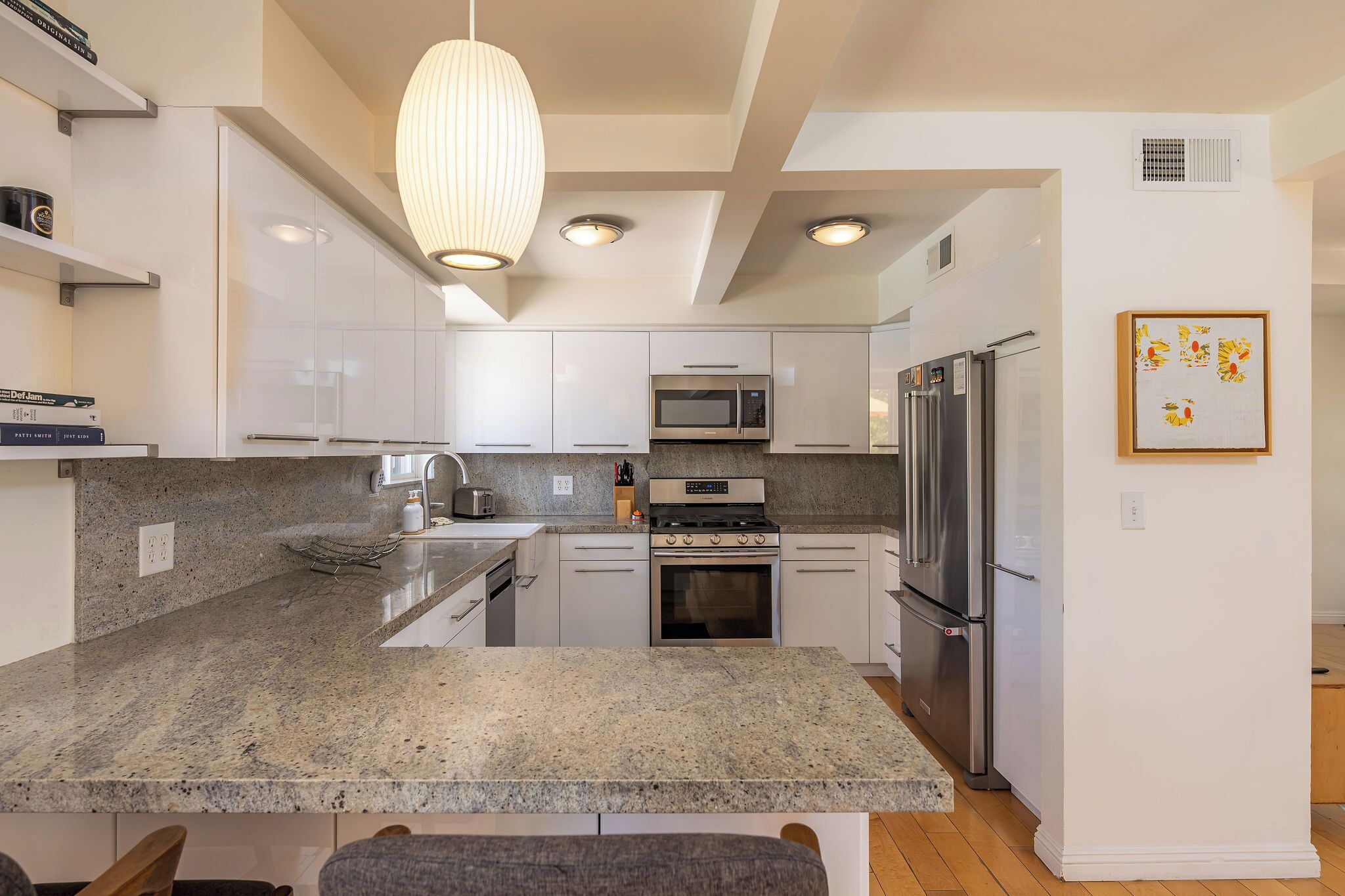 A modern kitchen with granite countertops, stainless steel appliances, and a pendant light.