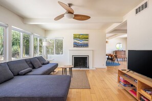 Un salon moderne avec un canapé, une cheminée, un téléviseur et un ventilateur de plafond.