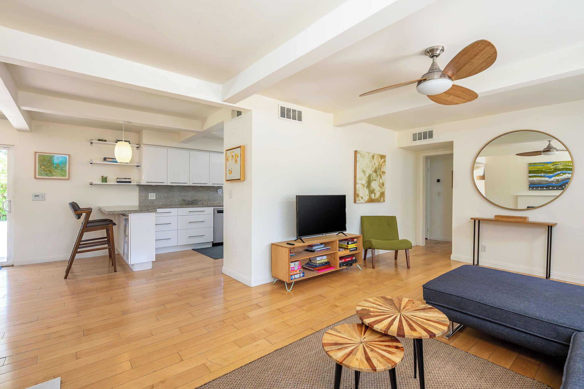 A modern living room with a sofa, a TV, a ceiling fan, and a kitchen in the background.