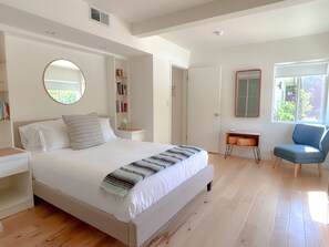 A bedroom with a large bed, a bedside table, a chair, a desk, a mirror, and a window. - Mid-Century Desert Oasis Private Pool & Spa (Palm Springs)