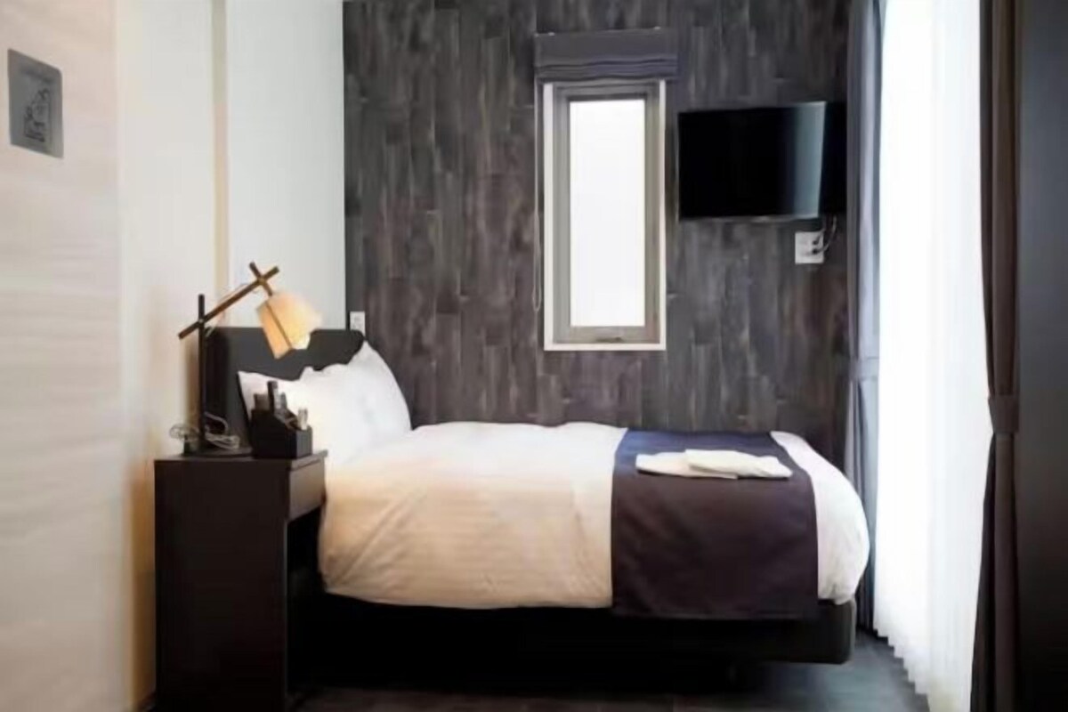 Una habitación de hotel moderna con cama, mesita de noche, lámpara y televisión montada en la pared.