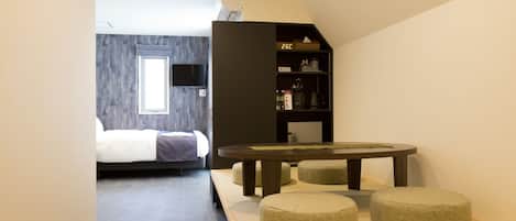 Una habitación de hotel moderna con una cama, una pequeña mesa de comedor y otomanas.