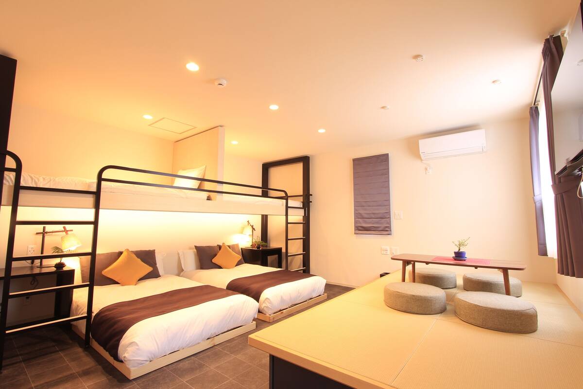 A hotel room with bunk beds, a small table, and a seating area with ottomans.