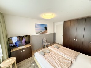 Una habitación de hotel con una cama, televisión, silla, escritorio y armario.