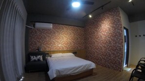 A bedroom with a brick wall, a bed, a nightstand, a chair, and a ceiling fan. - Dan Blue B&B (Magong)