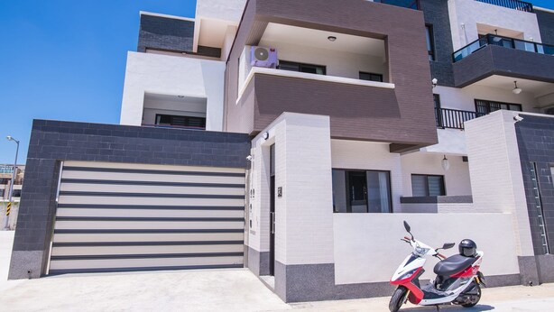 A modern multi-story building with a closed garage door, a parked scooter, and a clear blue sky. - Dan Blue B&B (Magong)