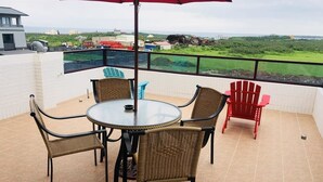 A terrace with a round table and wicker chairs, a red umbrella, and a view of the landscape. - Dan Blue B&B (Magong)