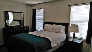 A hotel room with a bed, a dresser, a mirror, a nightstand, and a lamp.