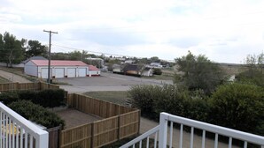 A residential area with a white building with a red roof, a fenced yard, and a road in the background.