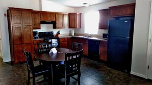 A kitchen with wooden cabinets, a black refrigerator, a stove, and a dining table with chairs.