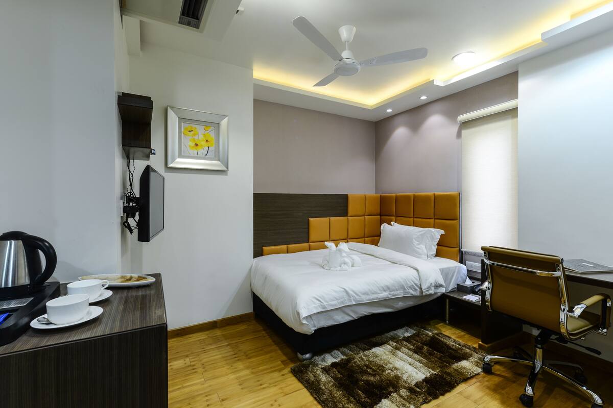 A modern hotel room with a bed, desk, and chair, a ceiling fan, and a framed picture on the wall.