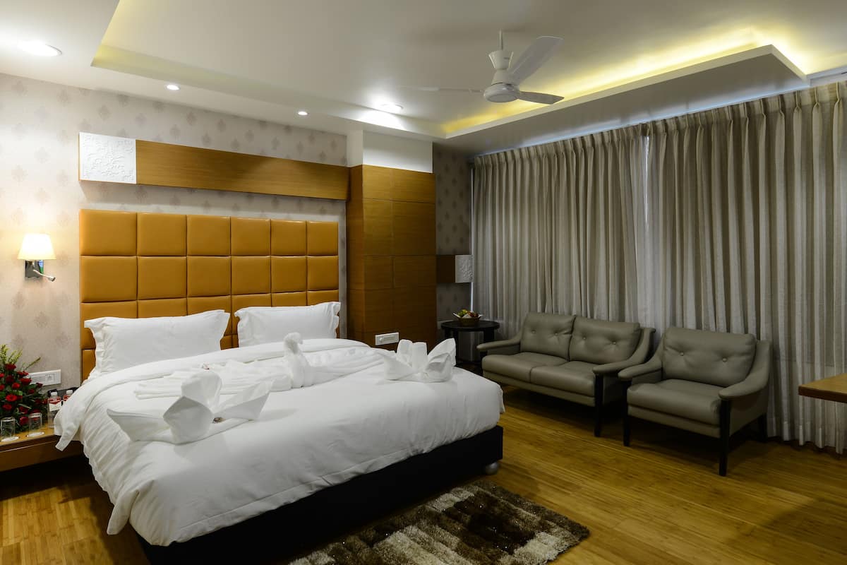 A hotel room with a large bed, a sofa, a small table, and a ceiling fan.