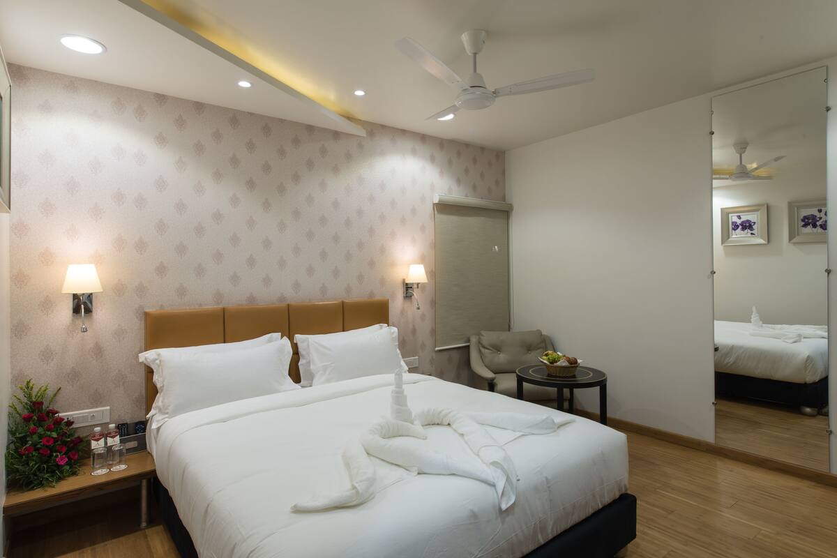 A hotel room with a bed, bedside lamps, a ceiling fan, a mirror, and a small table with a plant.