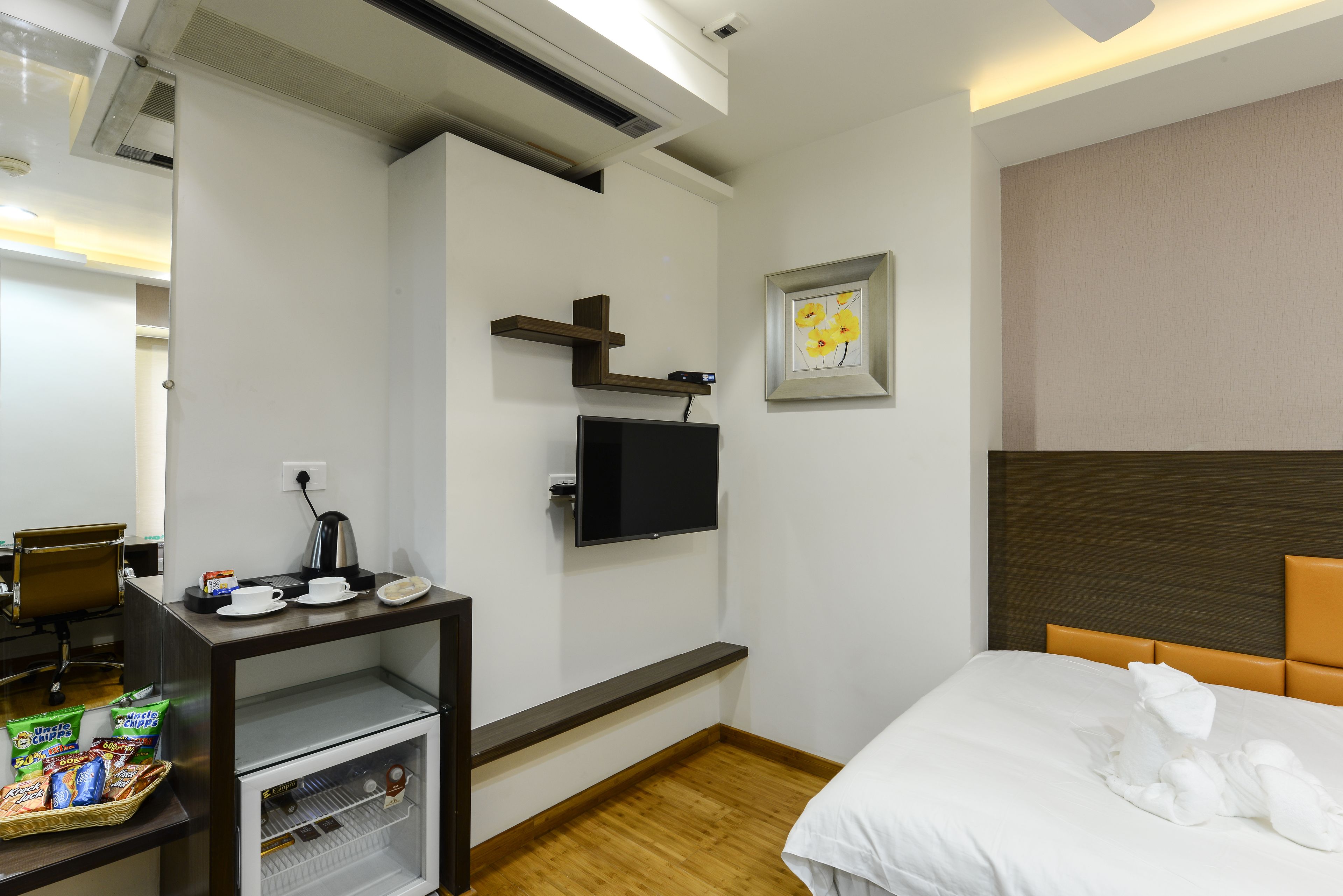 Una habitación de hotel con cama, escritorio con televisor de pantalla plana, cafetera y refrigerador pequeño.
