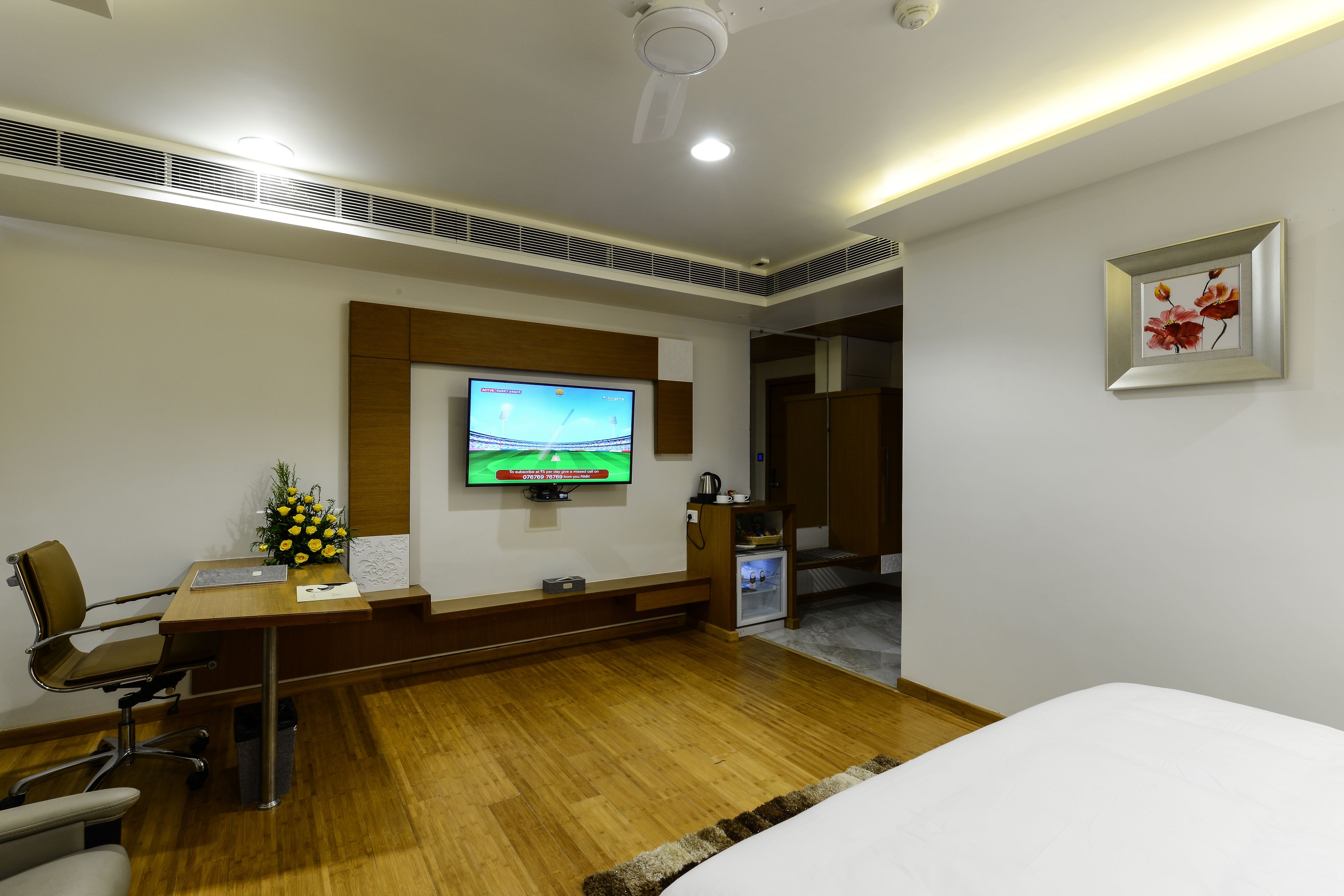 A hotel room with a wooden desk, a television, a bed, and a small kitchenette.