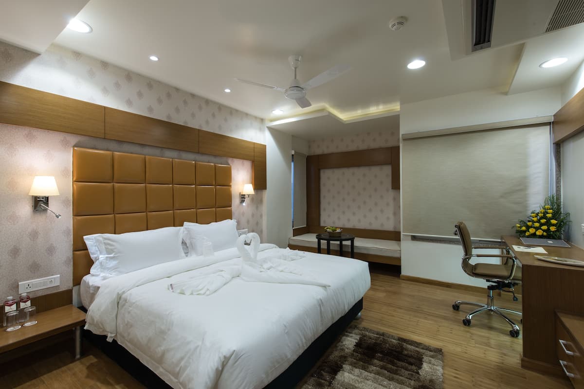 A hotel room with a large bed, a desk, a chair, and a small table.