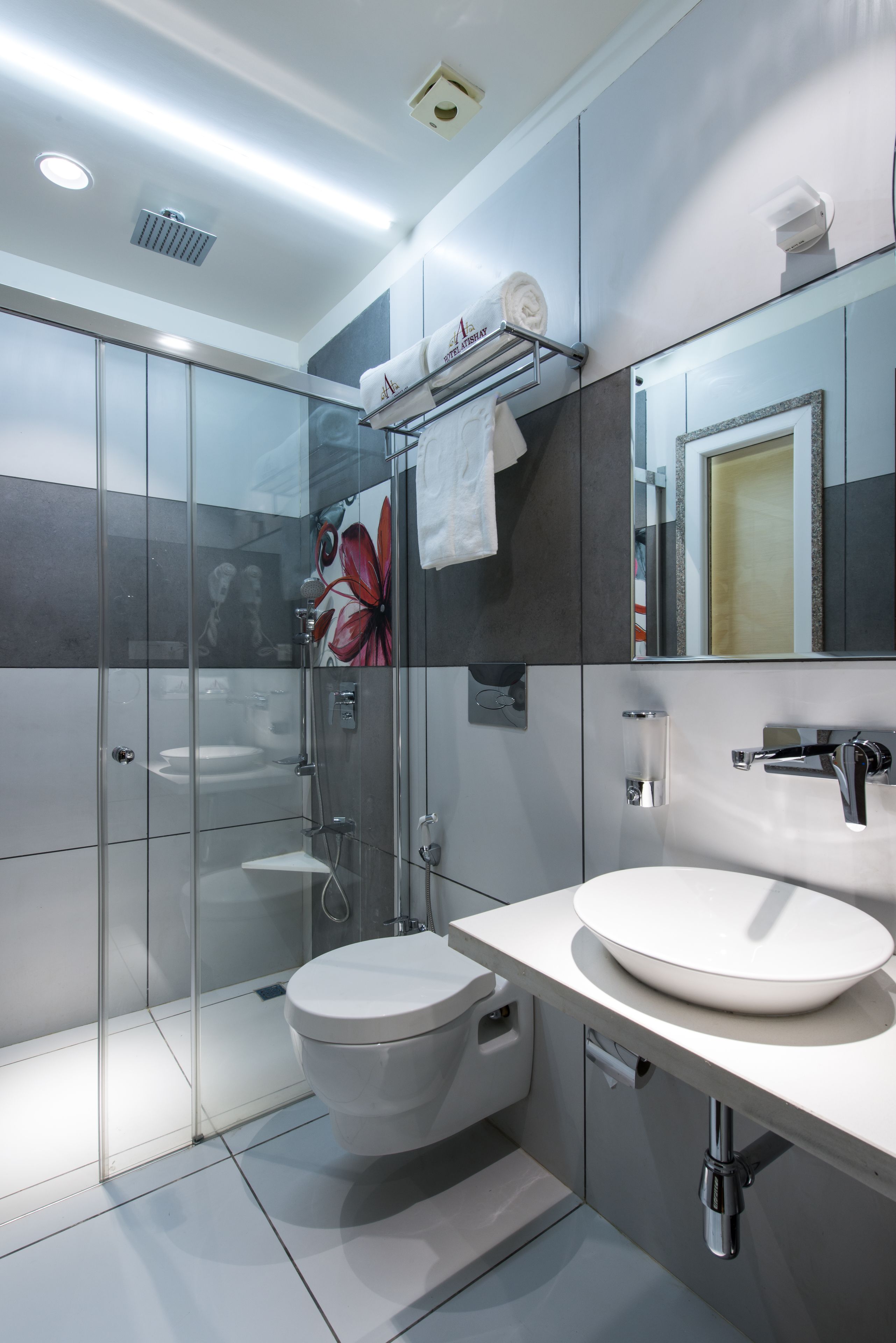 Un baño moderno con ducha de vidrio, un lavamanos blanco y un espejo grande sobre el tocador.