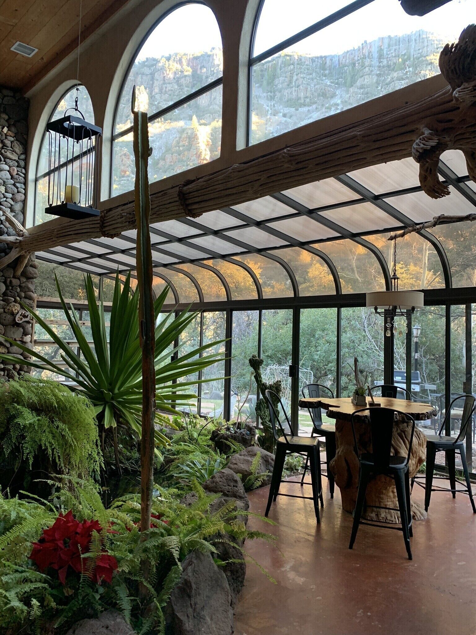 Une véranda avec un mur en pierre, de grandes fenêtres et une table en bois entourée de chaises.