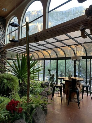 Ein Wintergarten mit Steinwand, großen Fenstern und einem Holztisch mit Stühlen.
