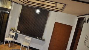 Une pièce avec une fenêtre munie de stores, une porte en bois et une petite table avec deux chaises.