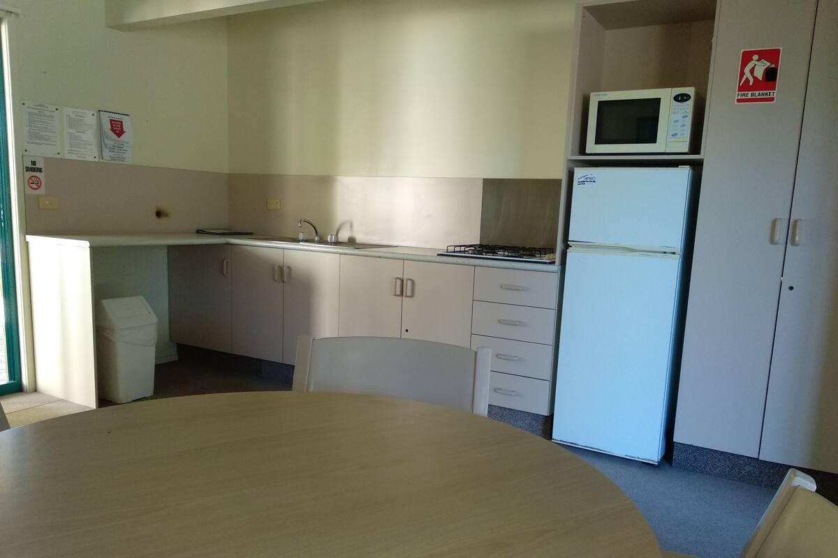 A compact kitchen with a microwave, stove, sink, and cabinets. There is a trash bin and a table with chairs.