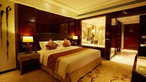 Habitación de hotel con una cama grande, dos mesitas de noche con lámparas, un espejo y vistas al baño.
