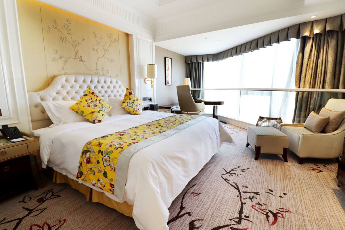 A hotel room with a large bed, a desk, a chair, and a view of the city.