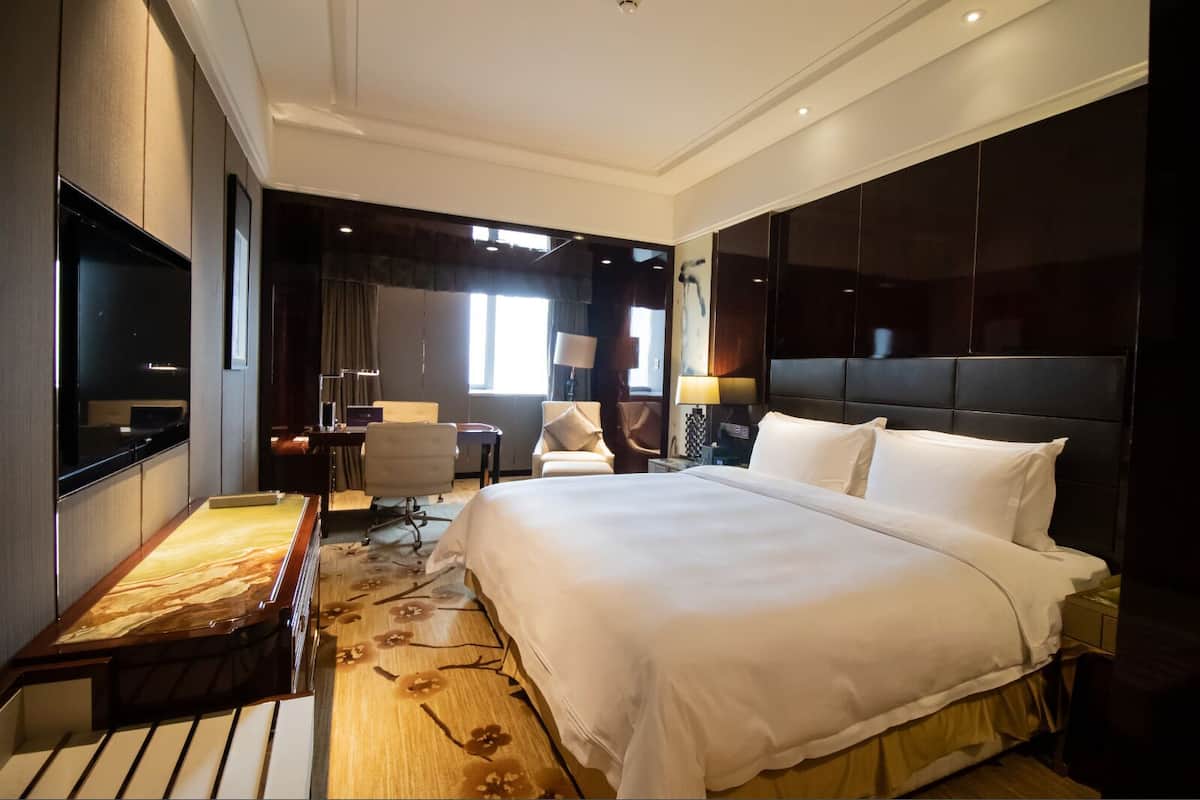 A modern hotel room with a large bed, a desk, a chair, and a TV.