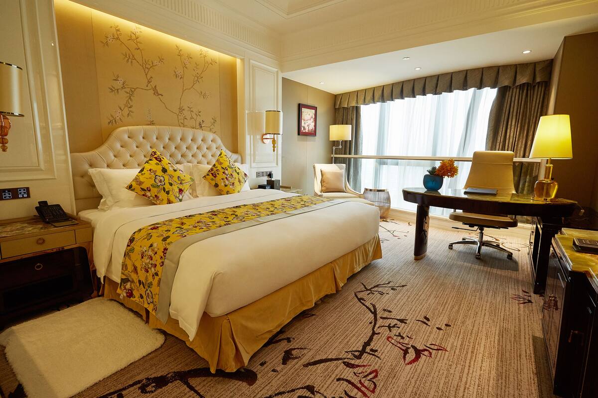A hotel room with a large bed, a desk, a chair, and a window with curtains.