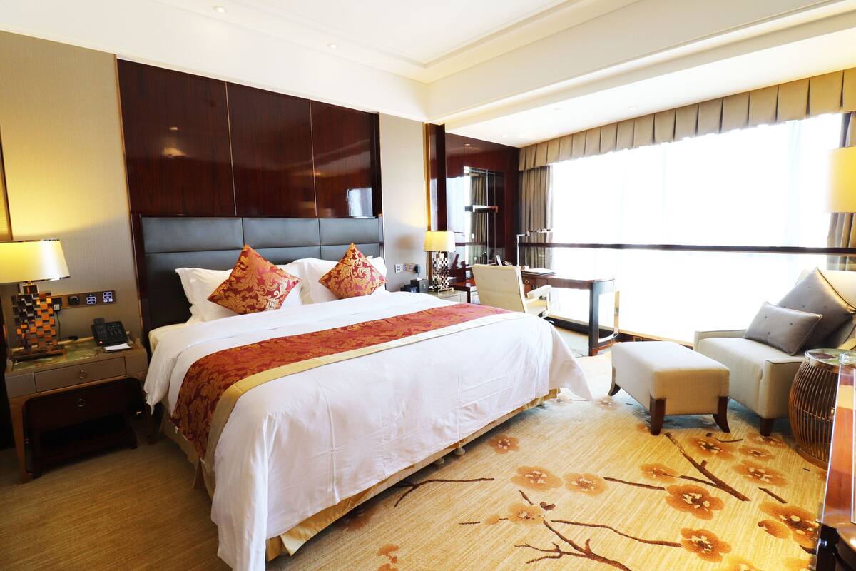 A hotel room with a large bed, a desk, a chair, and a view of the city.