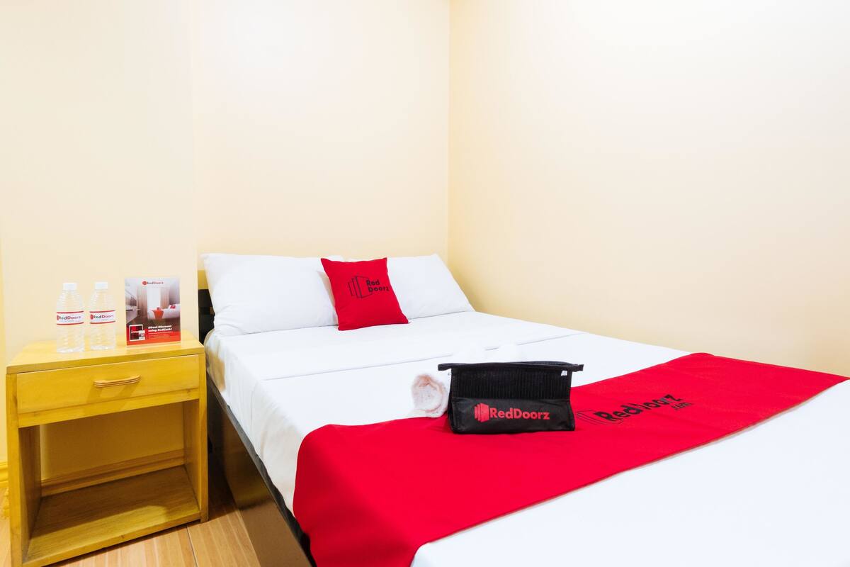 A hotel room with a bed, a nightstand, and a RedDoorz bag on the bed.