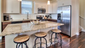 A modern kitchen with granite countertops, stainless steel appliances, and a central island with stools. - Whale of a Tale - Oyhut Bay Seaside Village (Ocean Shores)