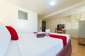 A hotel room with a bed, a desk, a television, and a refrigerator. - RedDoorz @ Ledesco Avenue Lapaz Iloilo (Iloilo)