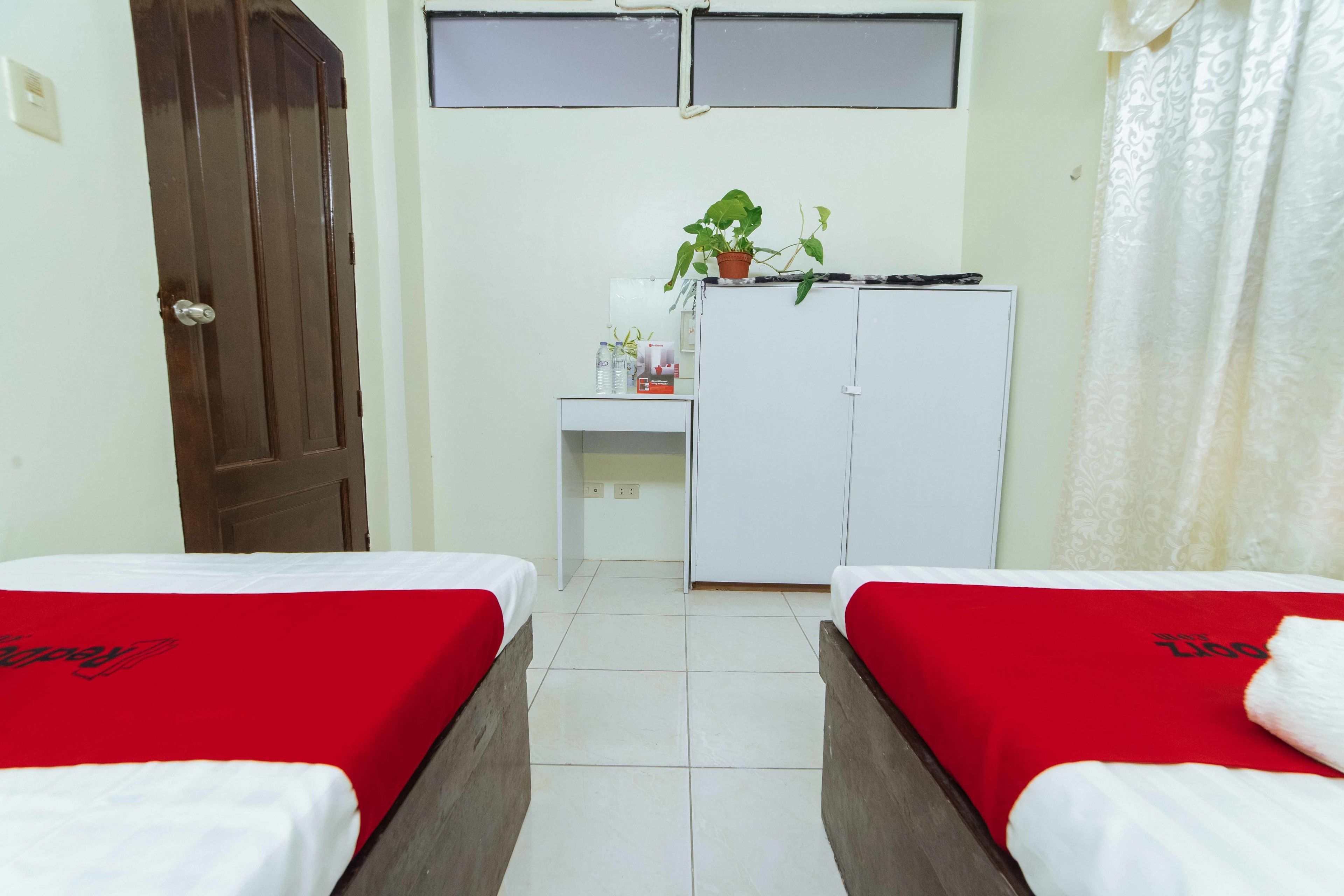 A room with two beds, a desk, a wardrobe, and a potted plant.