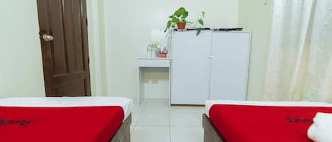 A room with two beds, a desk, a wardrobe, and a potted plant.