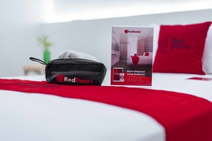 A neatly made bed with a red blanket, a black bag labeled 'RedDoorz', and a RedDoorz promotional box. - RedDoorz @ Ledesco Avenue Lapaz Iloilo (Iloilo)