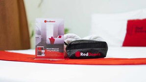 A RedDoorz branded bag and a promotional poster on a bed with a red blanket.