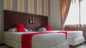 A hotel room with two beds, each with white bedding and red pillows, a wooden headboard, a bedside table with a lamp, and a window with curtains. - RedDoorz @ Cikutra 3 (Bandung)