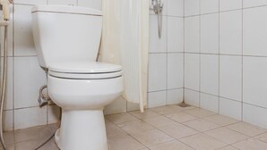 A white toilet with a shower attachment in a bathroom with white tiled walls and floor. - RedDoorz @ Cikutra 3 (Bandung)