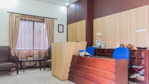 A reception area with a wooden desk, blue chairs, a sofa, and a window with curtains. - RedDoorz @ Cikutra 3 (Bandung)