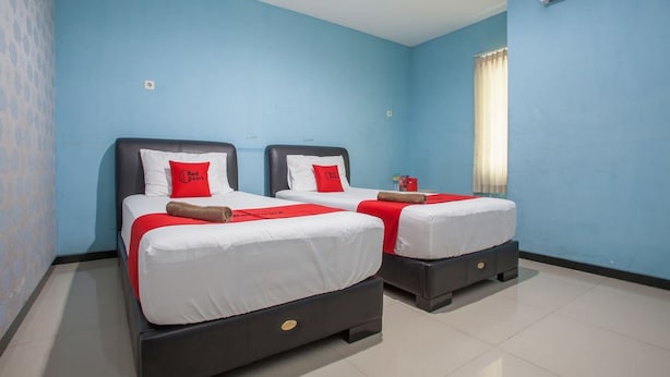 A hotel room with two beds, each with white bedding and red accents, against a blue wall. - RedDoorz @ Raya Tidar (Malang)
