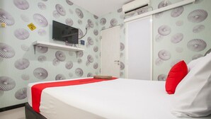 A hotel room with a bed, a TV mounted on the wall, a wardrobe, and a door. - RedDoorz @ Raya Tidar (Malang)
